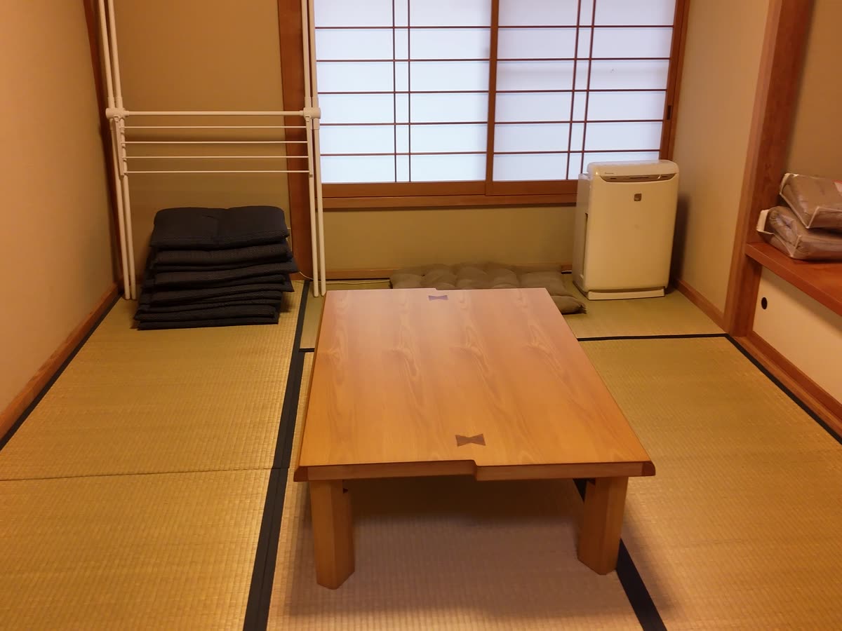 座卓と、隅に積んだ座布団。奥は障子