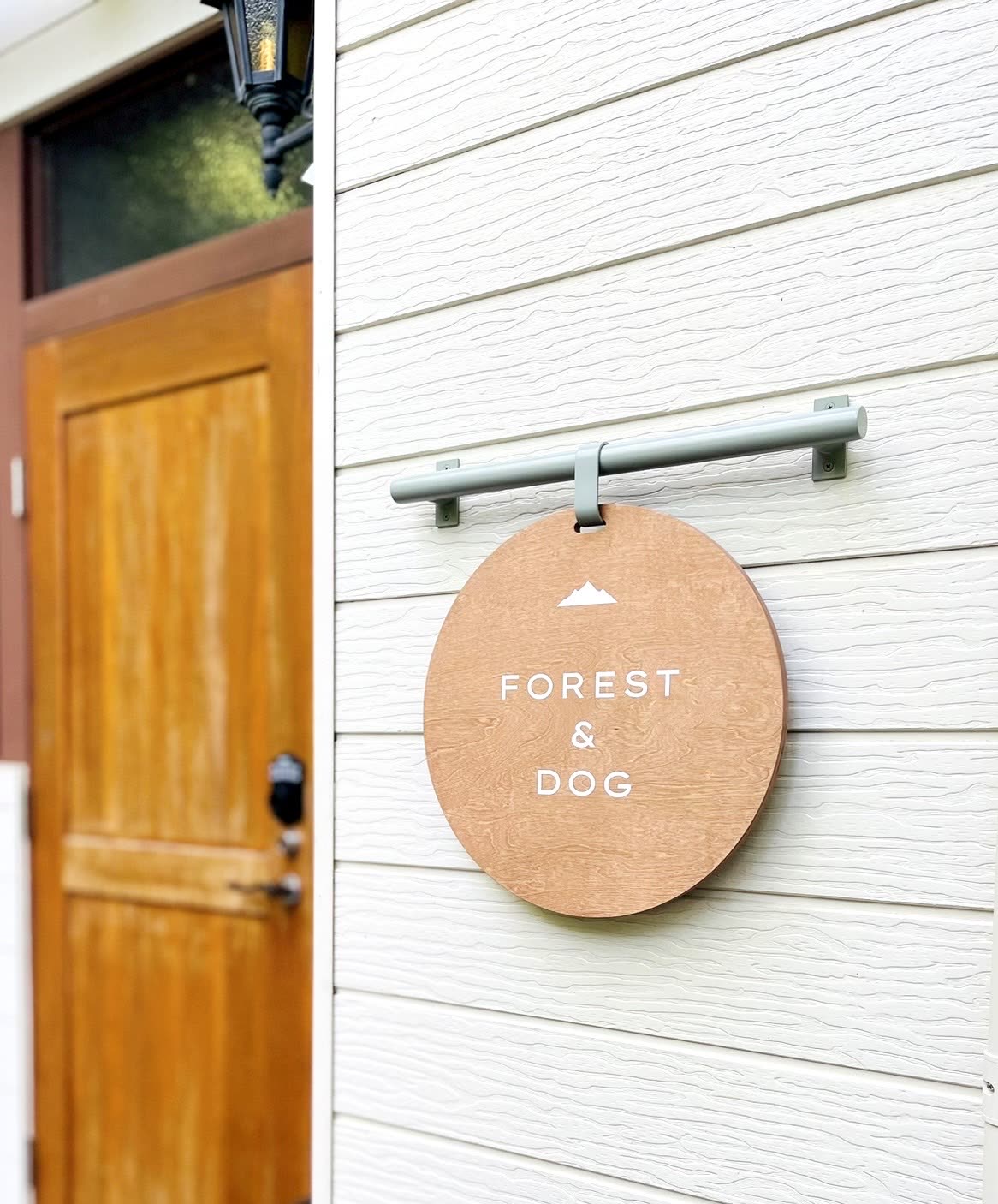 白い外壁に掛かる、山のマークとFOREST & DOGの文字が入った丸い木の看板